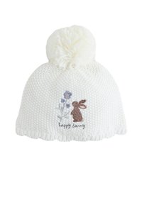 Witte gebreide muts met een grote crèmekleurige pompon bovenop, met een geborduurde bruine konijn en paarse bloemen en de tekst "happy bunny".