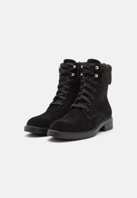 Stivaletti neri in suede con colletto in pelliccia sintetica, caratterizzati da un design con lacci e dettagli in metallo argentato sulla parte anteriore. Tacco a blocco.