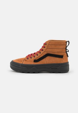 Baskets montantes en suede marron avec des accents noirs, lacets rouges, panneaux latéraux texturés et une semelle en caoutchouc noire avec un motif de semelle.