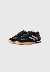 Chaussures de sport noires présentant une combinaison de matériaux lisses et texturés, avec une accent en imprimé serpent et une semelle en caoutchouc gomme.