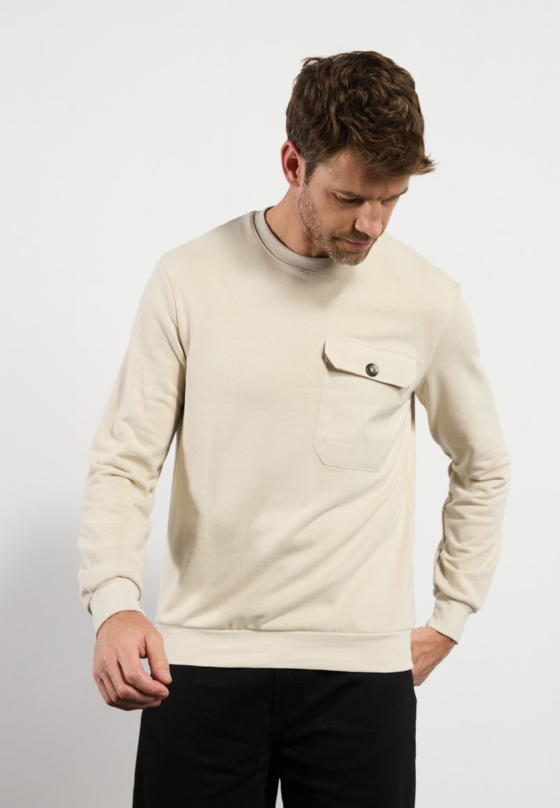 Lichtbeige sweatshirt met een ronde hals, lange mouwen en een voorzak met een drukknop. Gladde textuur en casual pasvorm.