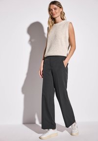 Top senza maniche di colore beige chiaro abbinato a pantaloni larghi grigi scuri. La modella indossa sneakers bianche. Tessuto testurizzato con una vestibilità comoda.