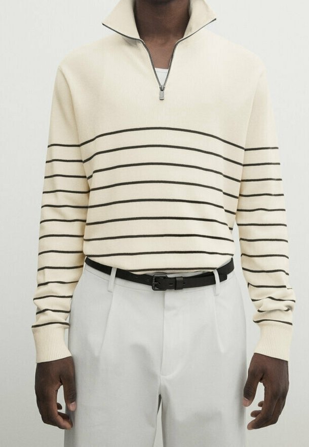Pull crème à rayures horizontales noires, col zippé, coupe ajustée, assorti à un pantalon gris clair et une ceinture noire.