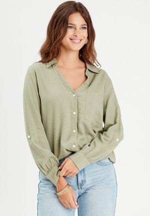 Light green blouse with long sleeves, button closure, and a pocket. Made of soft fabric, featuring a relaxed fit and roll-up cuffs.