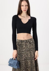 Top negru scurt, cu decolteu în V și textură pliată, asortat cu o fustă cu imprimeu leopard și o geantă mică din suede albastru.