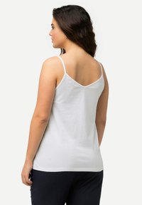 Weißes Baumwoll-Top mit dünnen Trägern, V-Ausschnitt und schlichter Textur. Kombiniert mit einer dunklen Hose, die eine lockere Passform zeigt.