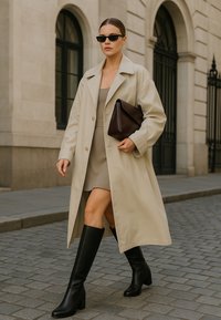 Beige trenchcoat, grijze jurk, zwarte kniehoge laarzen en een donkerbruine tas. Strakke zonnebril en een rechte silhouet. Kasseienstraat.