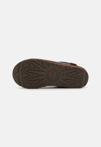 Brown rubber shoe sole with a textured pattern, featuring ridges and a circular emblem at the heel for enhanced grip and stability.
