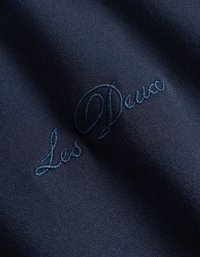 Ναυτικό ύφασμα με απαλό υφή και κεντημένο λογότυπο "Les Deux" σε σκούρο μπλε, που αναδεικνύει μία διακριτική γυαλάδα και καθαρό σχέδιο.