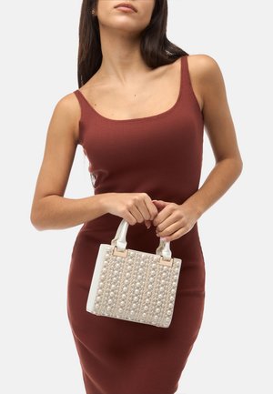 Witte handtas met parelaccenten, gestructureerde vorm, bovenhandvatten en beige hardware, gecombineerd met een bordeauxrode ribbeljurk.