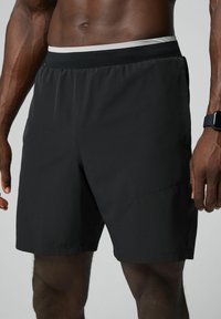 Schwarze sportive Shorts mit flachem Bund, Seitentaschen und einer leichten, glatten Textur. Mit einem kontrastierenden weißen Akzent am Bund.