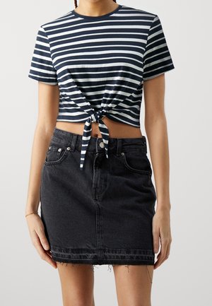 Camiseta corta a rayas en azul marino y blanco con nudo al frente; combinada con una falda mini de mezclilla negra con dobladillo deshilachado y diseño de cinco bolsillos.
