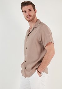 Kortærmet, beige skjorte lavet af letvægtsstof, med en afslappet pasform, sorte knapper og et fladt kravedesign.