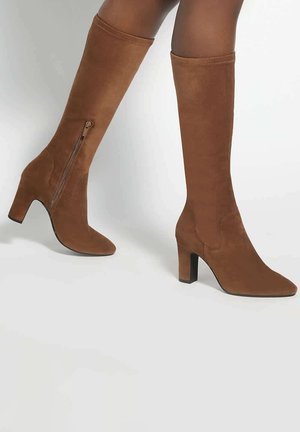 Brown suede knee-high boots with block heels and side zippers worn on legs against a plain background.