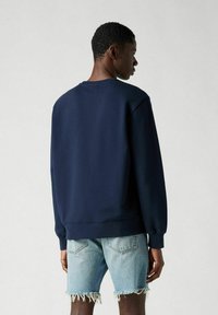 Marine sweatshirt met een ronde halslijn en geribbelde manchetten, gemaakt van zacht materiaal. Gecombineerd met lichte denim shorts met rafelige zoom.