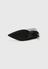 Bottines en cuir noir à bout pointu, au design épuré et à talon fin. Texture lisse avec un minimum de détails.
