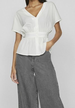 Blouse blanche à manches courtes avec un col en V, taille cintrée et fermetures à boutons, associée à un pantalon large taille haute gris clair.