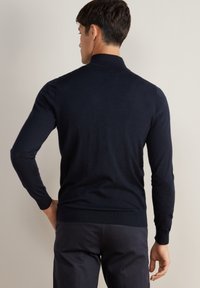 Granatowy sweter z wysokim kołnierzem, długimi rękawami i ściągaczami. Miękka tekstura, dopasowany krój, minimalistyczny styl. Dobrze przylega w talii.