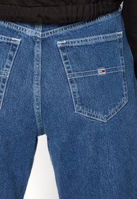 Jeans de mezclilla azul con un corte clásico, que cuentan con dos bolsillos traseros y una pequeña etiqueta de logo en rojo, blanco y azul en el bolsillo derecho.