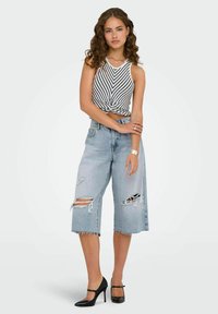 Top a righe corti abbinato a jeans larghi strappati di colore blu chiaro. Tacchi alti neri completano l'outfit.