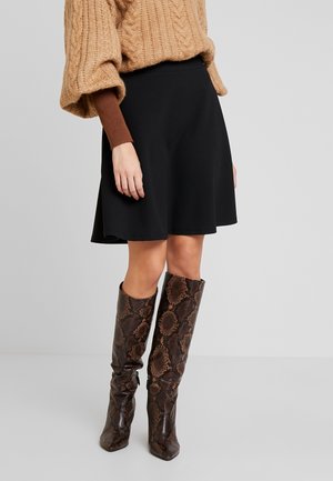 Mujer vistiendo una falda negra de corte en A, un suéter de punto grueso oversize color marrón claro y botas altas hasta la rodilla con estampado de piel de serpiente en marrón.