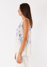 Top senza maniche floreale realizzato in un tessuto leggero e trasparente. Presenta motivi blu e crema, una vestibilità comoda e un orlo arrotondato.