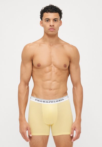 Rumene bombažne bokserice s belim elastičnim pasom, na katerem je napis "POLO RALPH LAUREN", prileganje, gladka tekstura.