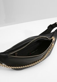 Marsupio in pelle nera con dettaglio in catena dorata, apertura con zip e foderatura in tessuto. Presenta una tracolla regolabile per indossarlo.