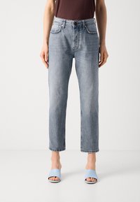 Helleblaue gerade geschnittene Jeans aus Denim, mit fünf Taschen, Gürtelschlaufen und einem Knopfverschluss; getragen mit hellblauen Rutsch-Sandalen.