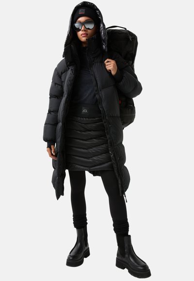 Black puffer coat with a hood, layered over a textured black skirt. Worn with black leggings and chunky ankle boots, complemented by oversized sunglasses.