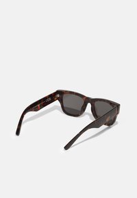 Lunettes de soleil en écaille de tortue avec des verres gris, monture carrée et branches droites. Présente des variations de motifs subtiles et des accents en métal sur les branches.
