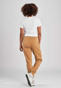 T-shirt bianco accorciato, pantaloni jogger beige con vita elastica e sneakers bianche con suole nere, viste da dietro. Texture del tessuto liscia.
