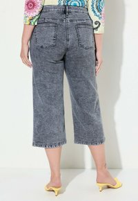 Pantaloni cropped grigi in denim con una texture sbiadita, dotati di tasche posteriori e vita media. Indossati con tacchi gialli.