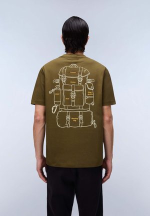 Person, die ein olivgrünes Hemd mit weißem Rucksack trägt, illustriert mit Wanderutensilien: Kamera, Kleidung, Wasser, Essen, Karte, Schlafsack.