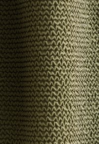 Gros plan d’un tissu texturé vert olive avec un motif tricot zigzag créant une surface tridimensionnelle.