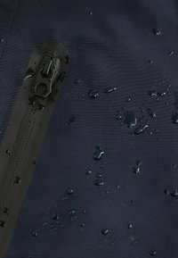 Navy wodoodporna tkanina o teksturowanym wykończeniu, z czarnym zamkiem błyskawicznym i kroplami wody na powierzchni dla skutecznej odporności na wilgoć.