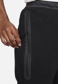 Schwarze Jogginghosen mit einer Reißverschlusstasche und einem strukturierten Naht. Der Stoff wirkt weich und hat einen leicht elastischen Bund.