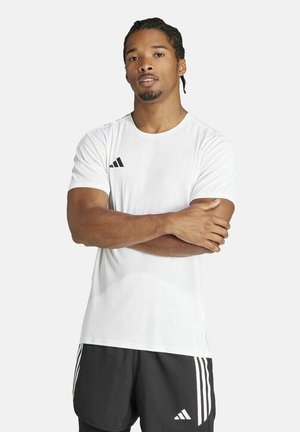 Athletic man with braided hair stands with arms crossed, wearing a white Adidas t-shirt and black Adidas shorts with white stripes.