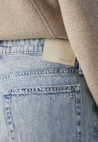 Jean en denim délavé clair avec un patch en cuir de la marque « rag & bone » et un logo « rb » brodé, associé à un pull en laine beige.