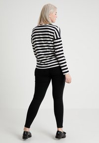 Maglietta a maniche lunghe a righe bianche e nere, vestibilità rilassata, abbinata a pantaloni skinny neri. L'outfit presenta un design minimalista e un tessuto morbido.