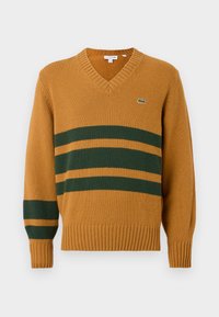 Mustard yellow V-neck sweater with dark green horizontal stripes across chest and left sleeve, featuring a small crocodile logo on the chest.