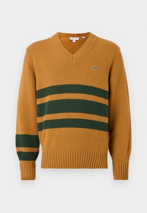 Mustard yellow V-neck sweater with dark green horizontal stripes across chest and left sleeve, featuring a small crocodile logo on the chest.