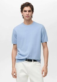 Ljust blå kortärmad t-shirt med rund halsringning, tillverkad av ett slätt tyg. Matchas med vita byxor och ett svart bälte. Enkel design, utan mönster.