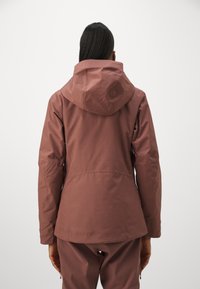 Vandtæt jakke i dæmpet pink, med hætte, lange ærmer og tætsiddende pasform. Glat tekstur med minimal detaljer på ryggen.