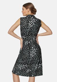 Ärmelloses schwarzes Kleid mit weißem und hellblauem gepunktetem Muster, knielang, mit flachem Kragen und figurbetonter Silhouette. Glatte Stofftextur.