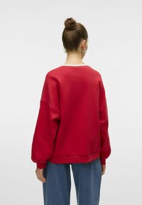 Sweatshirt rouge surdimensionné avec des manches longues et bouffantes et un col rond. Tissu doux à la texture lisse, avec une bordure de col blanche.