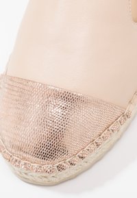 Gros plan sur une chaussure espadrille beige avec un capuchon de toe texturé en métal couleur or rose et des coutures de semelle en jute tressé.