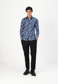 Camicia button-up floreale blu con varie sfumature di blu, bianco e nero. Abbinata a pantaloni neri e scarpe stringate nere.