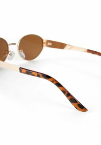 Round sunglasses with brown lenses, gold metal frame, and tortoiseshell-patterned temple arms. Textured nose pads for comfort.