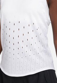 Débardeur blanc en tissu texturé avec des trous découpés de tailles variées, créant un effet dégradé. Ourlet arrondi et design sans manches.
